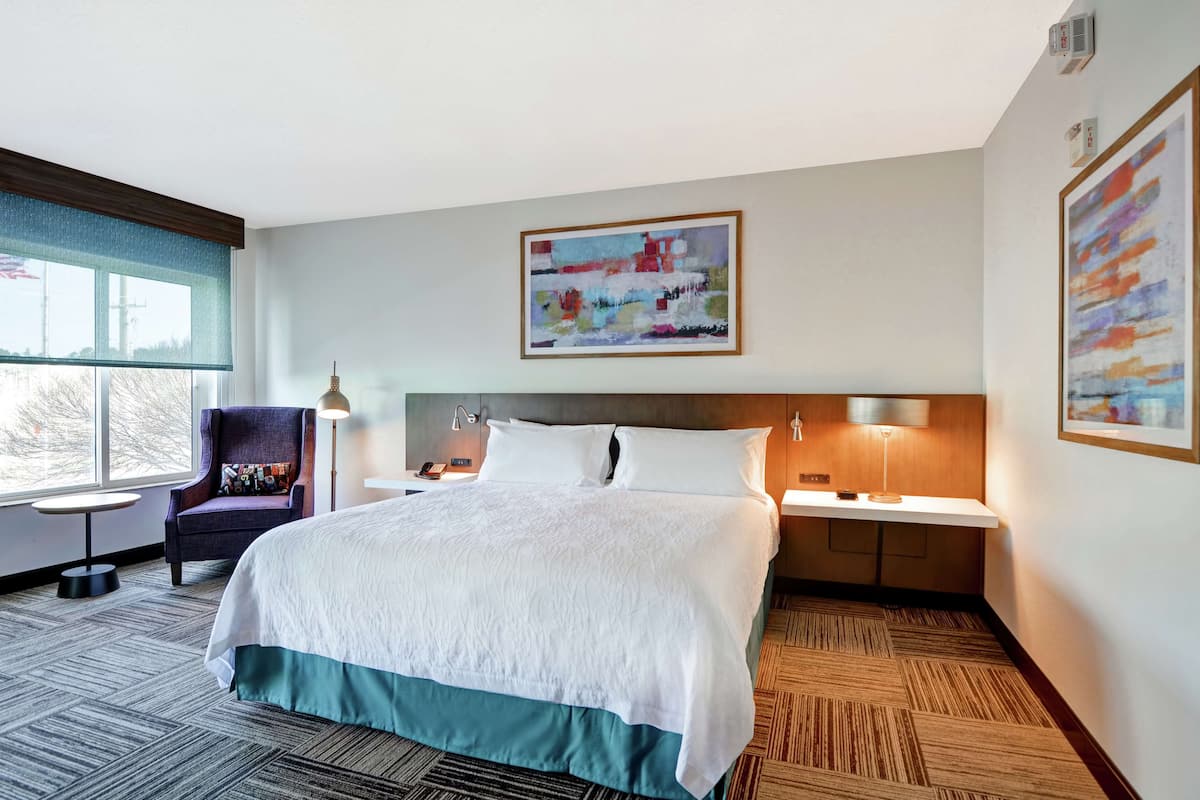 A hotel room with a large bed, a chair, a desk, and a window.