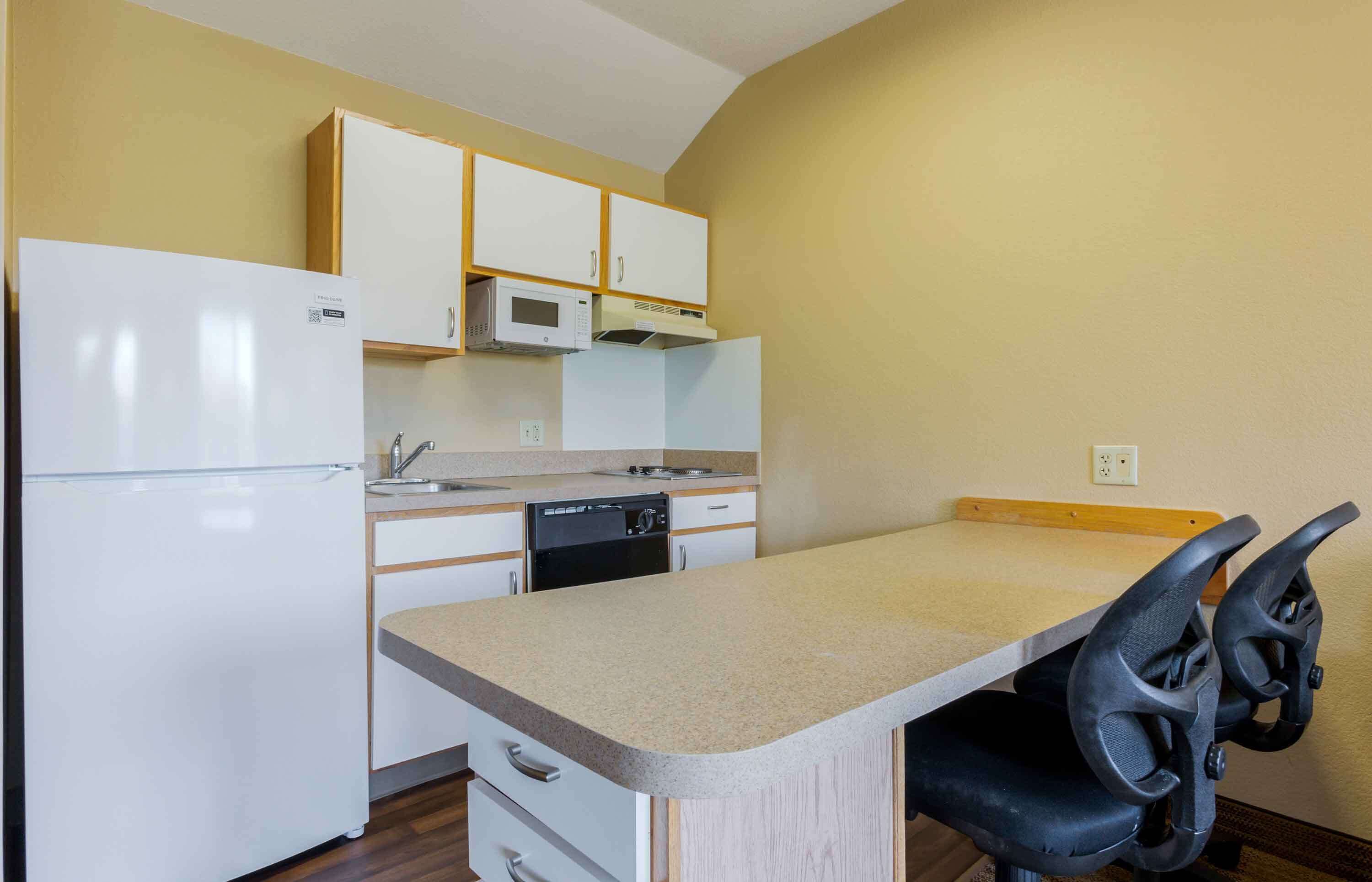 Cocina compacta con refrigerador, microondas, lavavajillas y un pequeño comedor con una silla.