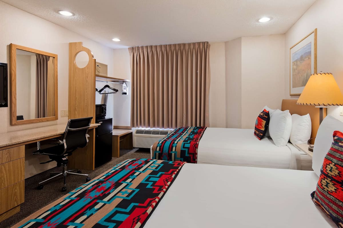 A hotel room with two beds, a desk with a chair, a television, and a window with curtains.