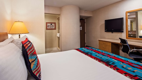 A hotel room with a bed, a desk, a chair, a television, and a shower area.