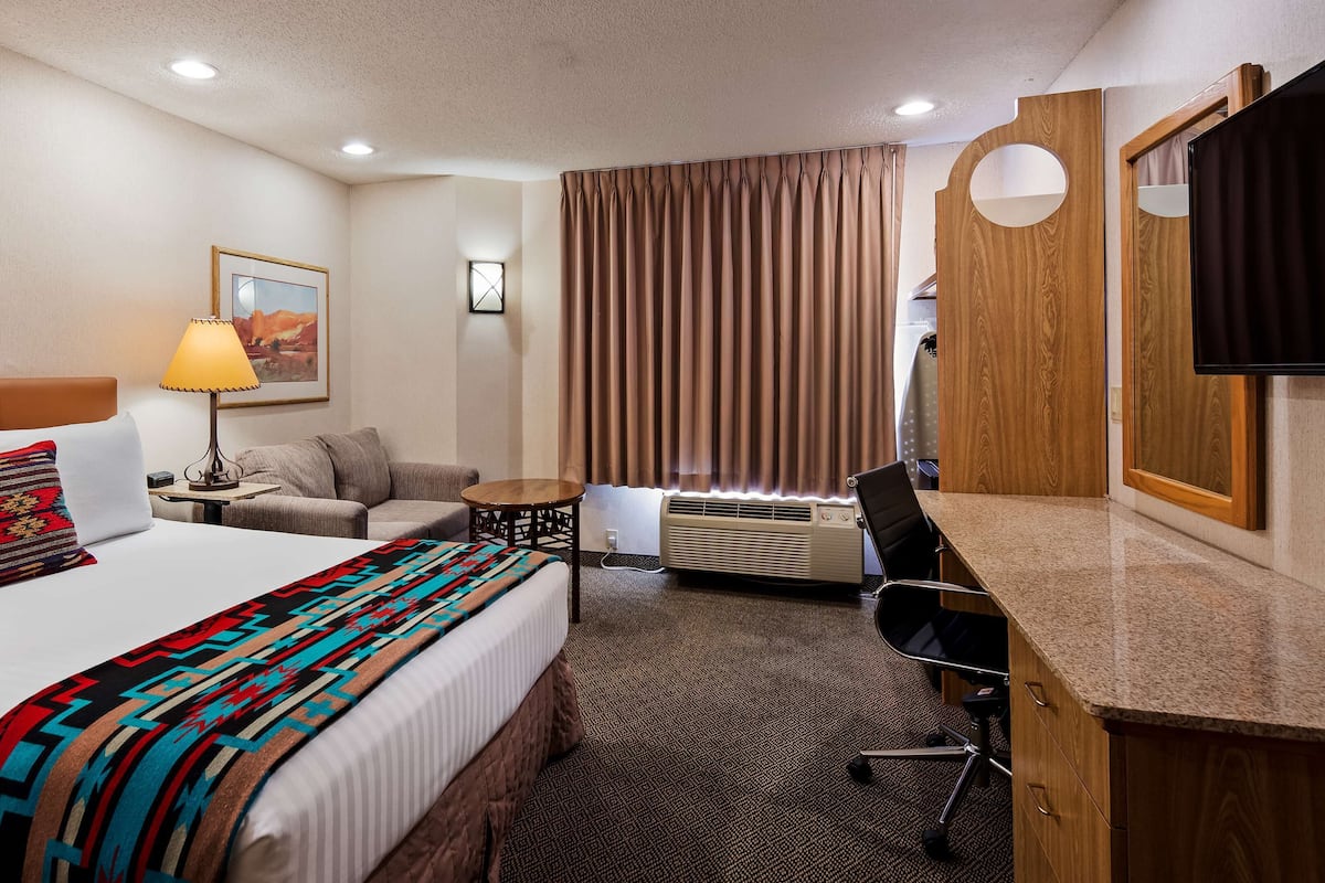 A hotel room with a bed, a desk, a chair, a lamp, a heater, and a television.