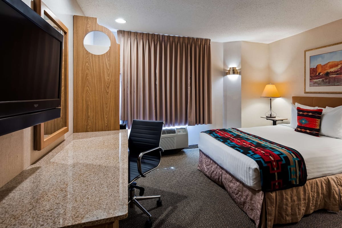 A hotel room with a bed, desk, chair, TV, and a painting on the wall.