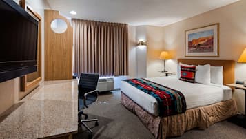Une chambre d’hôtel avec un lit, un bureau, une chaise, une télévision et un tableau au mur.