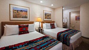 A hotel room with two beds, each with a patterned blanket, a nightstand with a lamp, and framed landscape paintings on the wall.