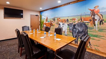 A conference room with a wooden table, black leather chairs, a flat-screen TV, and a mural of cattle on the wall.