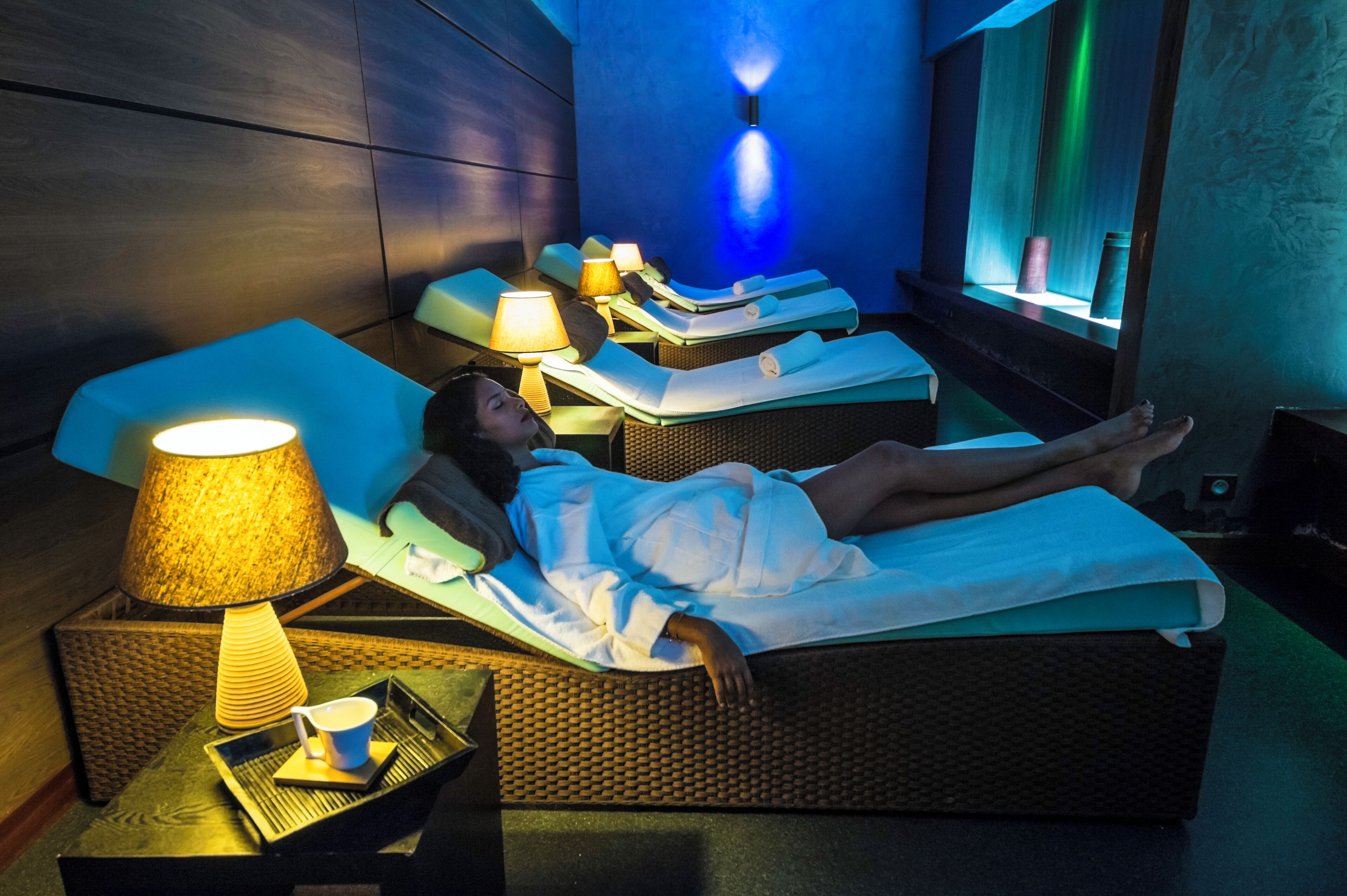 A spa room with massage beds, a massage table, a lamp, and a tray with a cup and saucer.