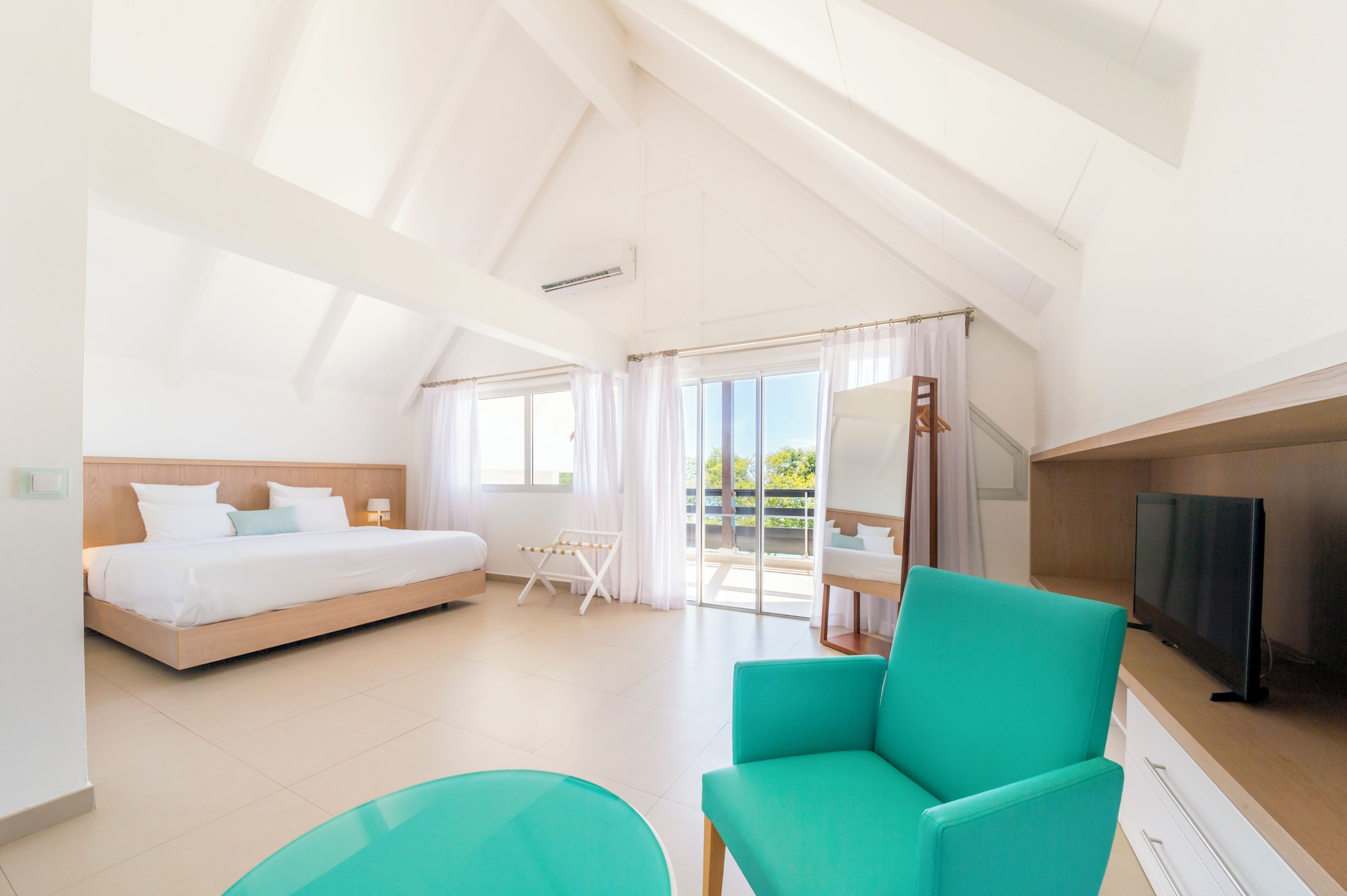 A modern hotel room with a bed, a TV, a seating area, and a balcony with a view.