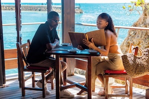 Two people seated at a wooden table with a view of the sea. - Mahogany Hôtel Résidence & Spa (Le Gosier)
