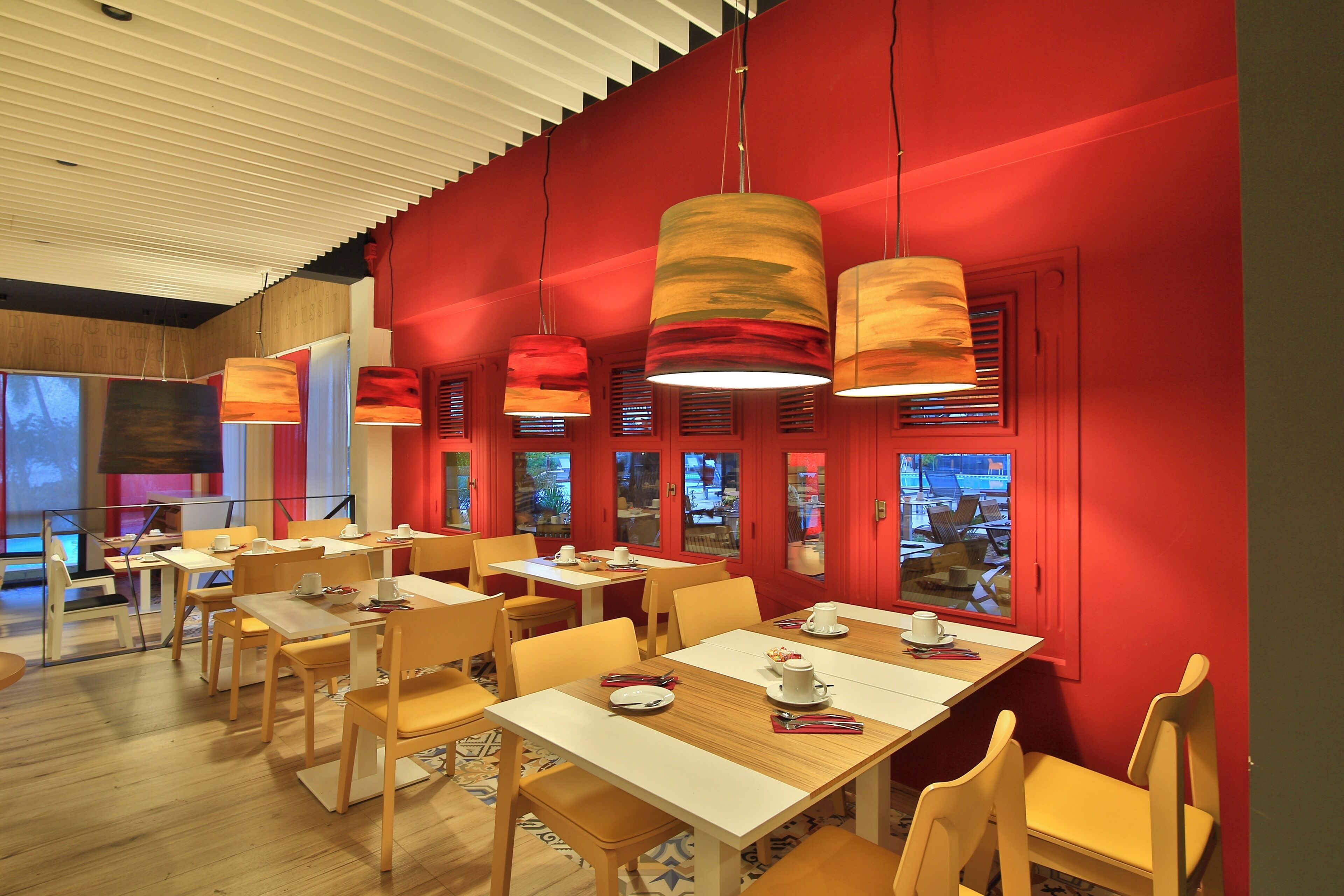 Un restaurante con mesas y sillas de madera, paredes rojas y lámparas colgantes.