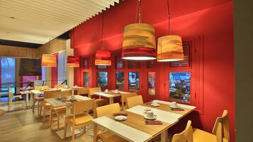 Un restaurante con mesas y sillas de madera, paredes rojas y lámparas colgantes.