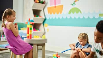 A child playing with building blocks at a table in a room with a colorful mural on the wall.