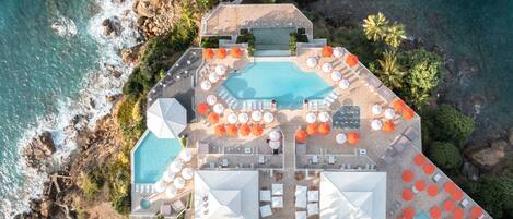 Vista aérea de un resort con una piscina grande, numerosas tumbonas y sombrillas.