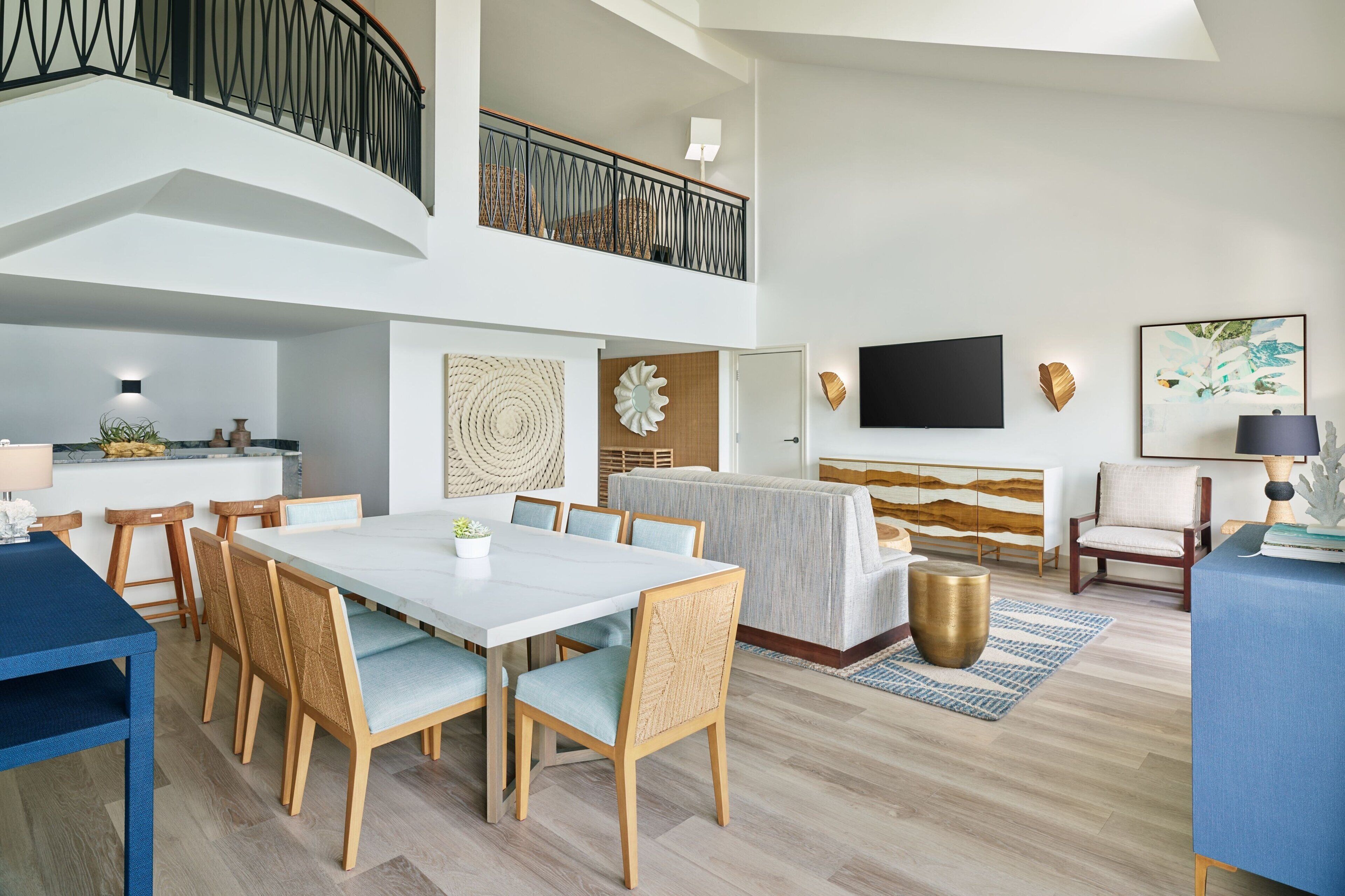 Een ruime woonkamer met een eettafel, stoelen, een bank en een aan de muur bevestigde televisie.