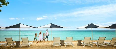 A beach with lounge chairs and umbrellas, a clear sky, and a calm sea.
