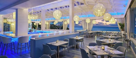 Un restaurant moderne doté d’un bar, de tables et de chaises, et offrant une vue sur la mer.