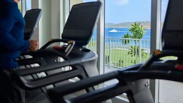 Una cinta de correr en una habitación con ventanas amplias que dan a un cuerpo de agua y un yate.