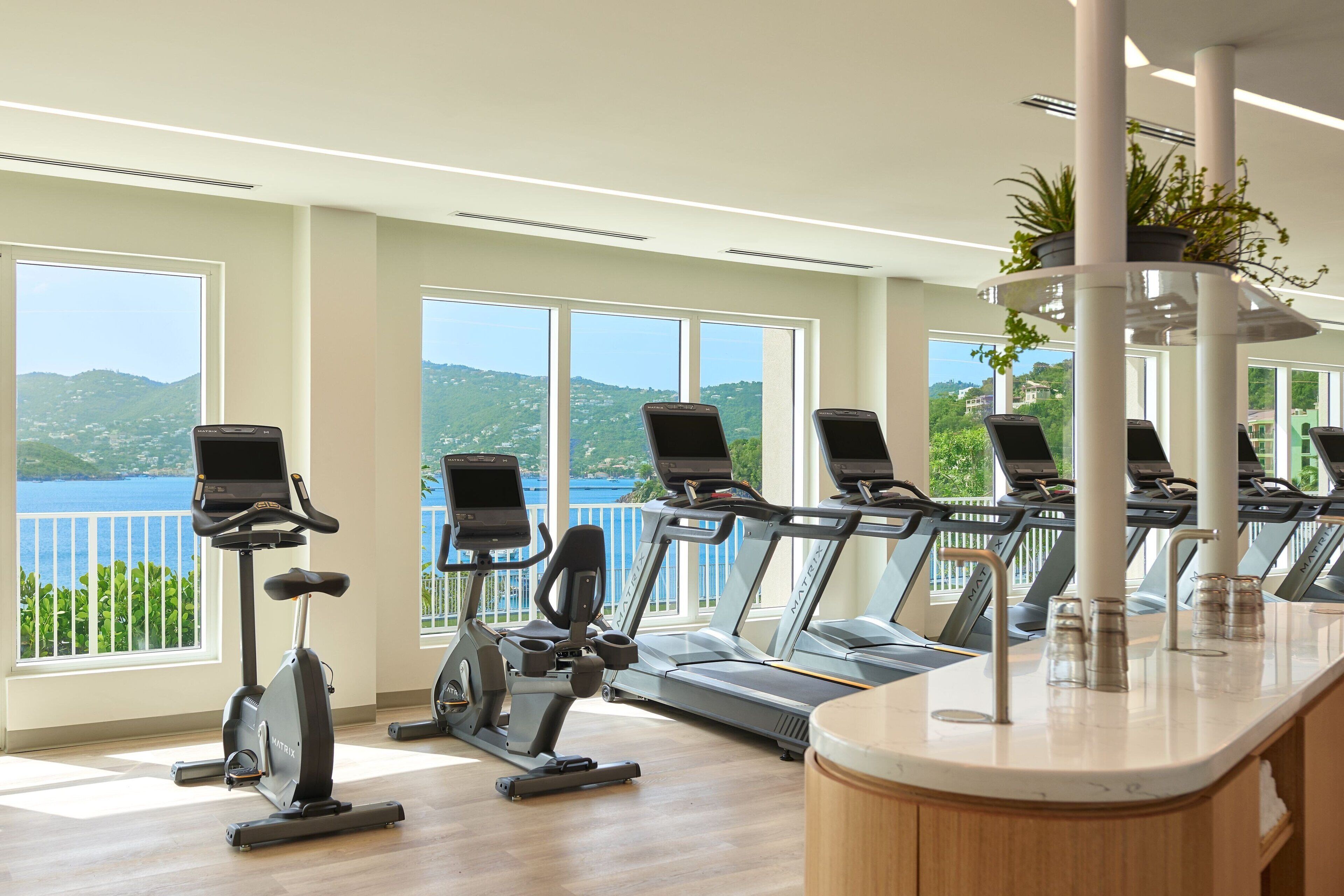 Un gimnasio con equipo de ejercicio, ventanas amplias y vistas al exterior.