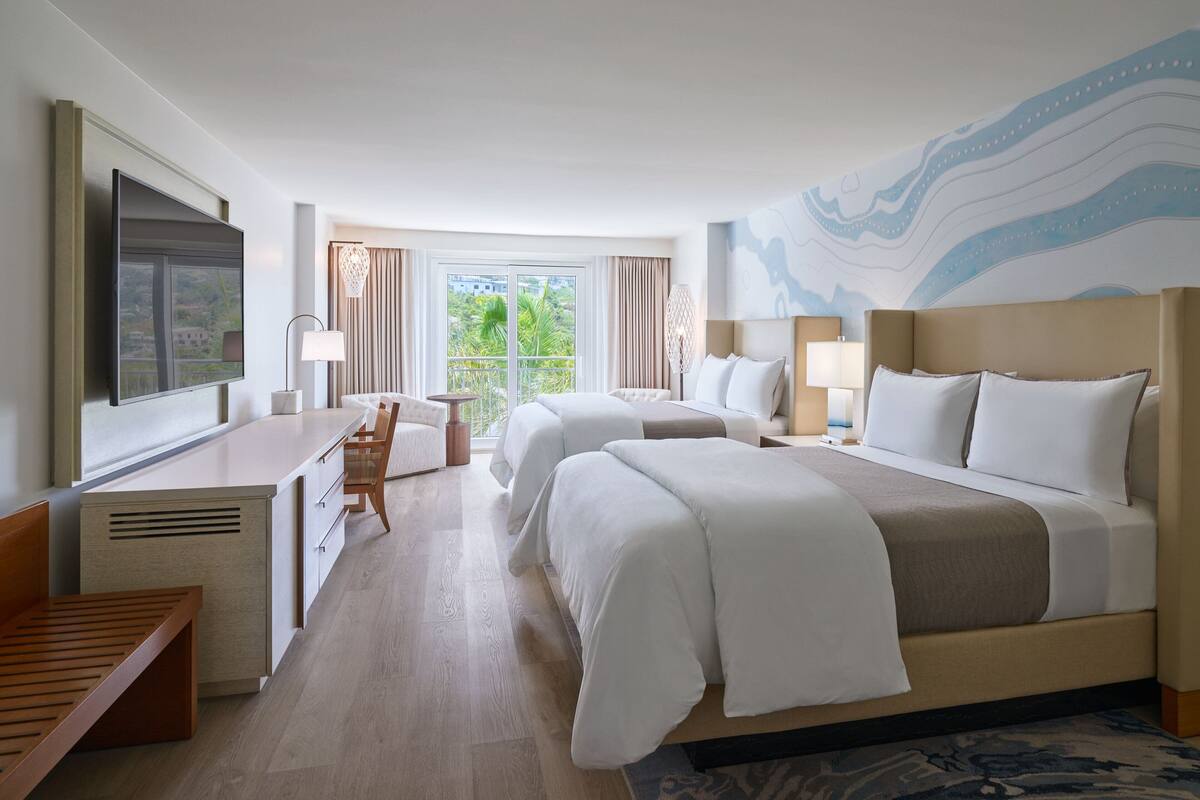 A hotel room with two beds, a desk, and a chair.