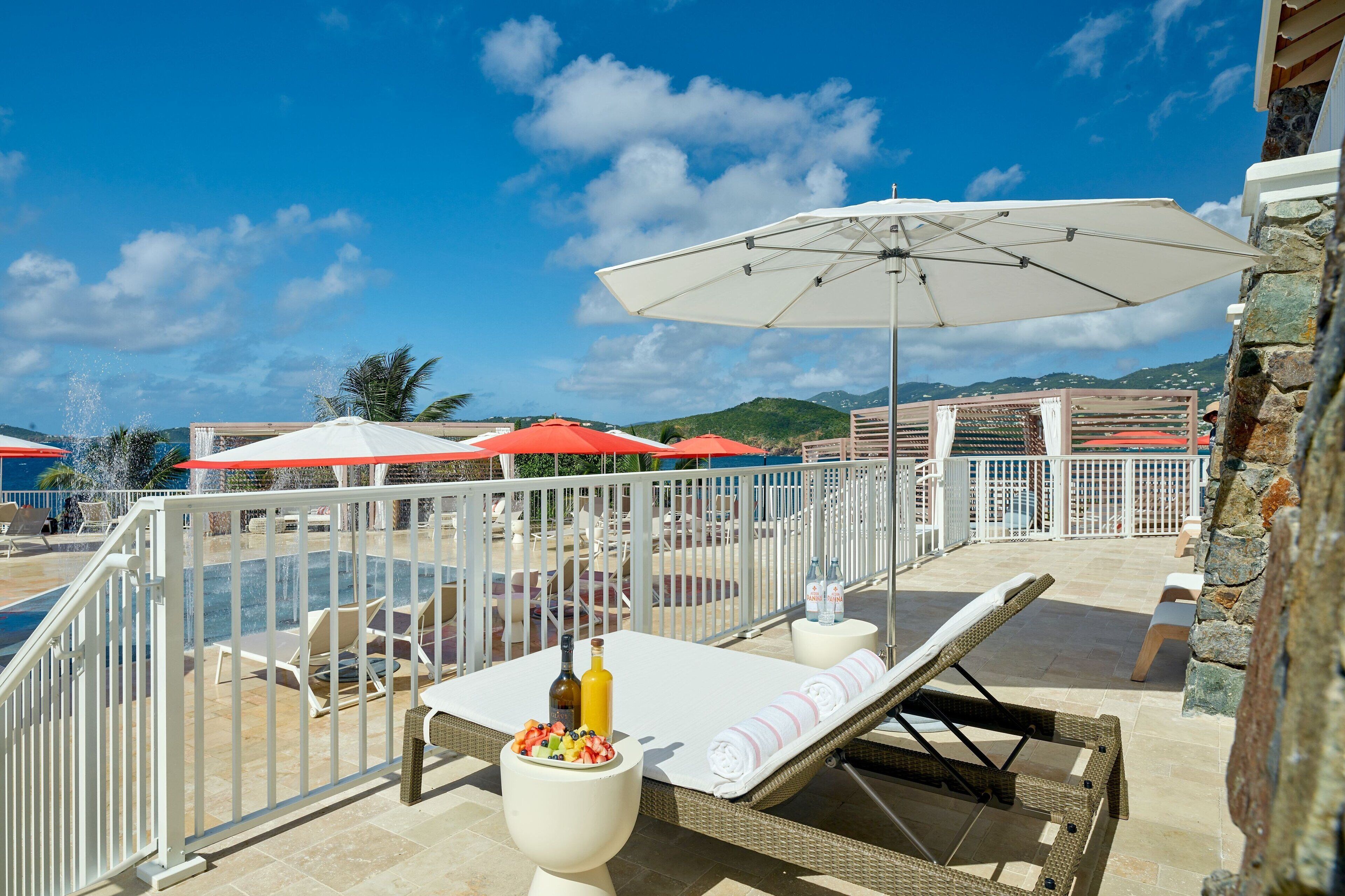 A poolside area with lounge chairs, umbrellas, and a table with a bottle and snacks.