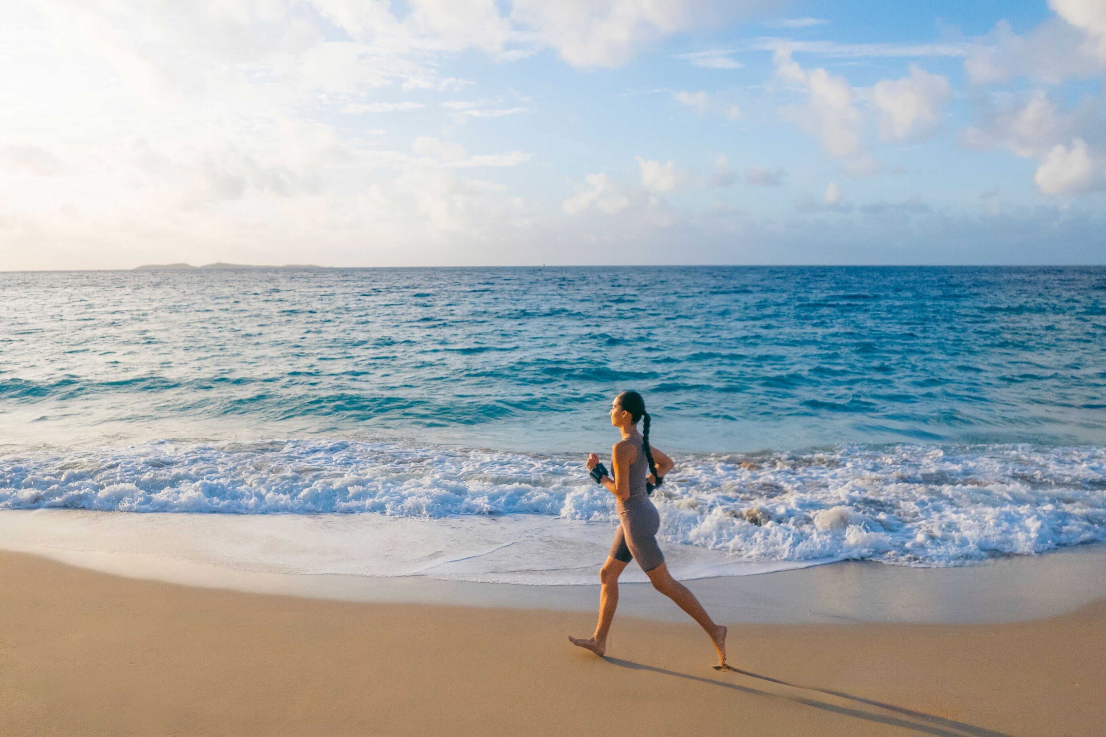 A person walking on a sandy beach with the ocean in the background.