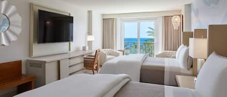 Habitación de hotel con dos camas, televisión, escritorio y vista al océano.