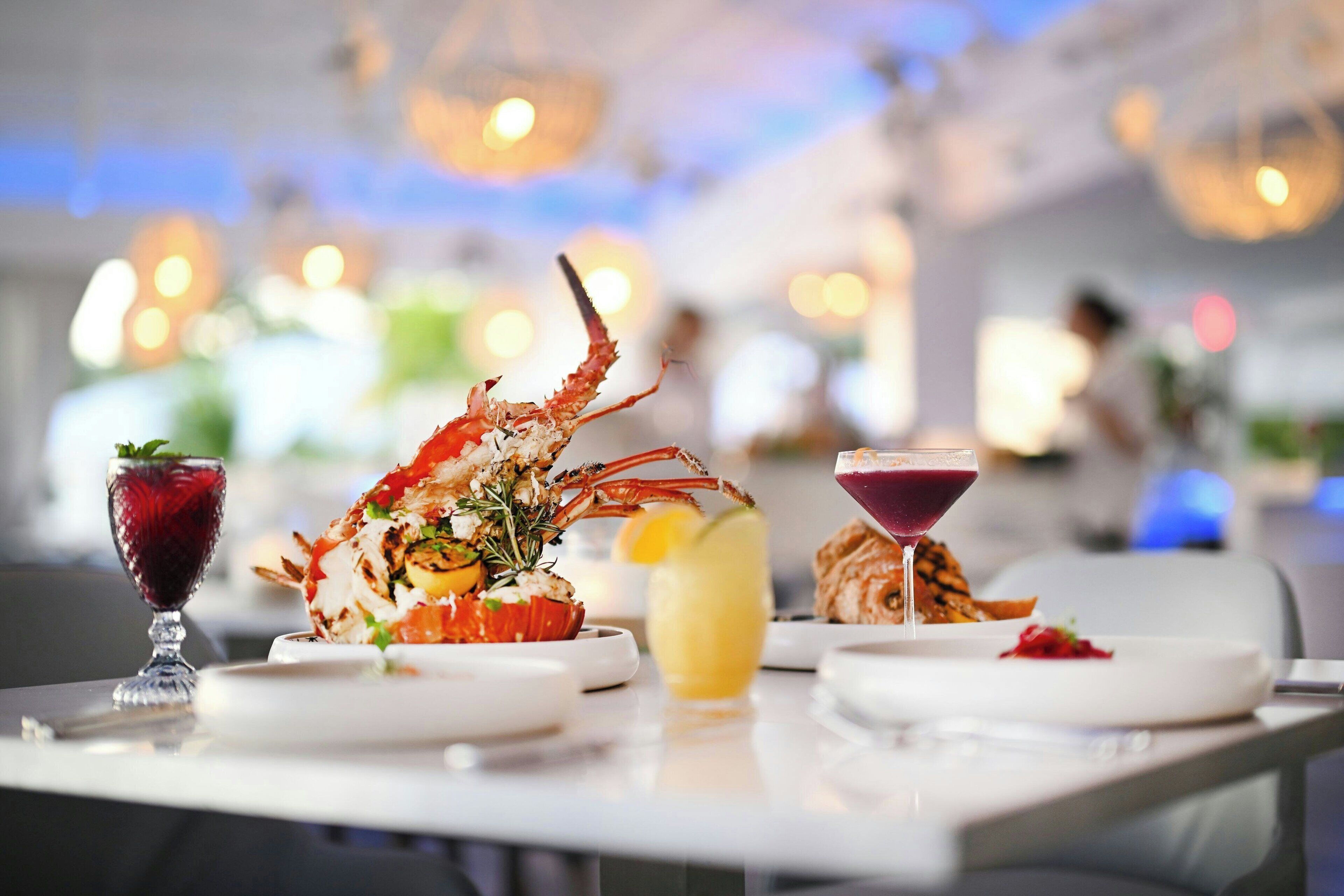 A dining table with a lobster dish, a glass of red drink, and a yellow beverage.