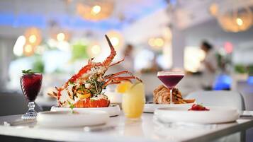 A dining table with a lobster dish, a glass of red drink, and a yellow beverage.