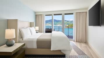 A hotel room with a large bed, a TV, a nightstand, and a view of a coastal landscape.