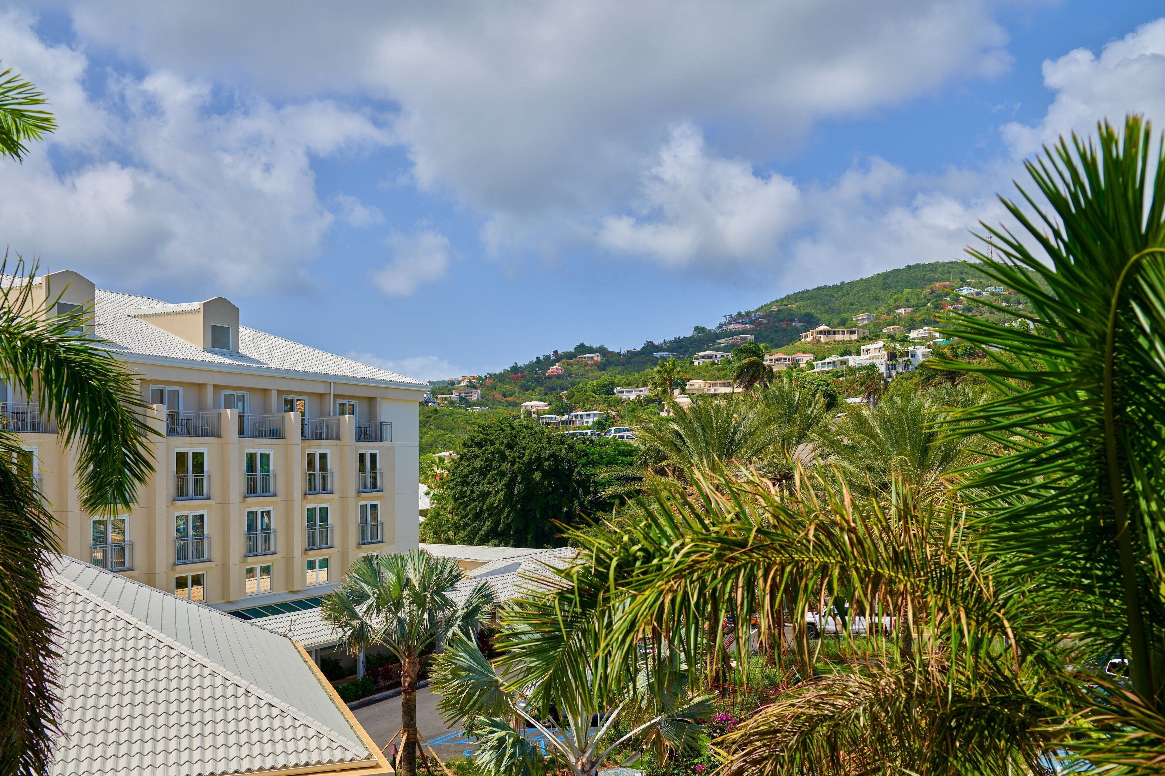 A hotel with multiple balconies, surrounded by lush greenery and a hilly landscape in the background.