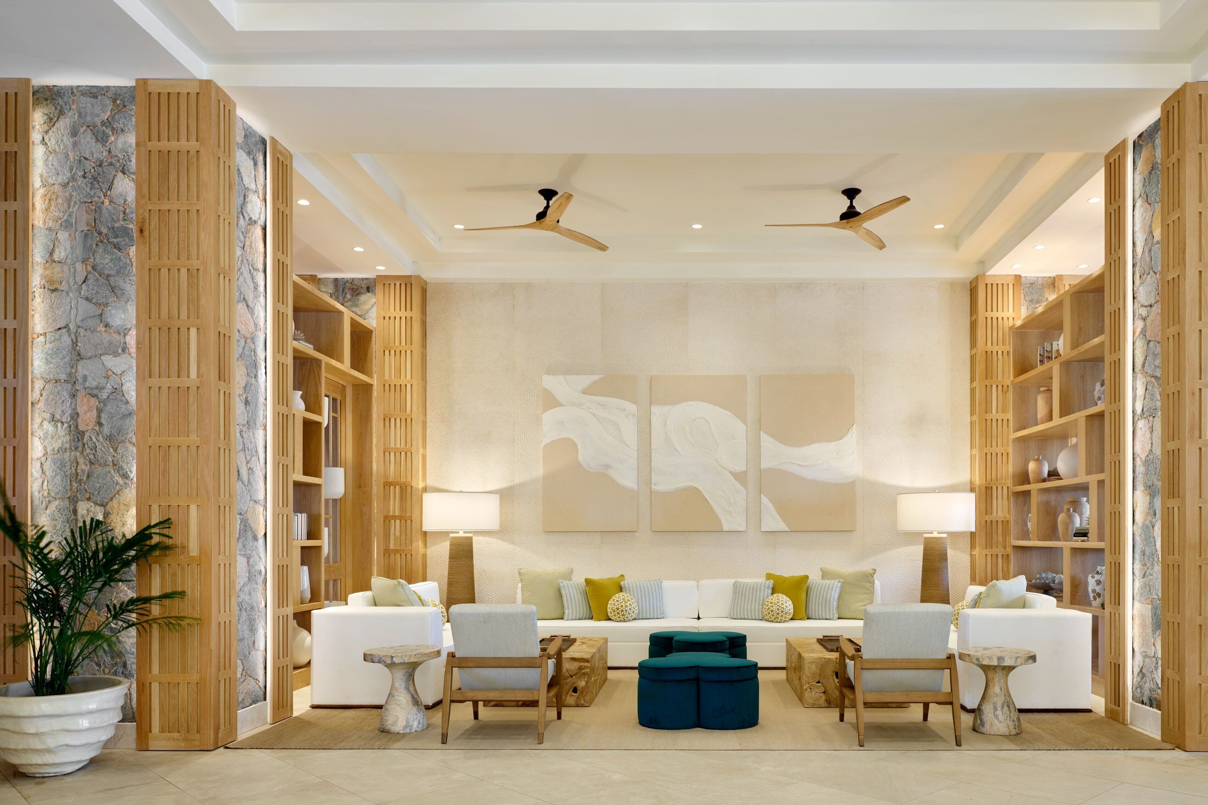 A spacious living area with a white sofa set, wooden shelving, and a large abstract painting on the wall.