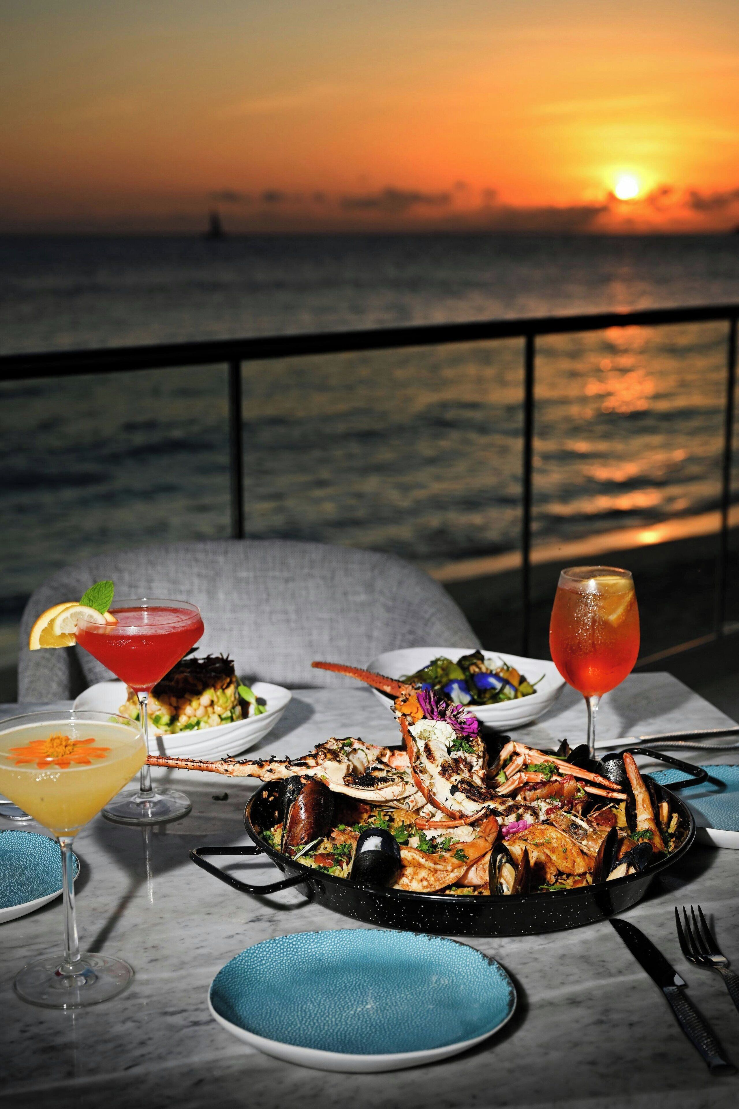 A seafood dish on a table with drinks and a sunset view.