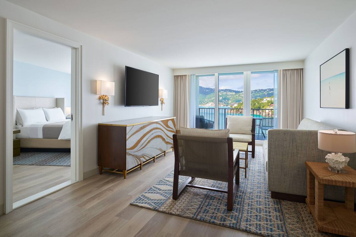 A hotel room with a bed, a desk, a chair, a TV, and a balcony with a view of the landscape.