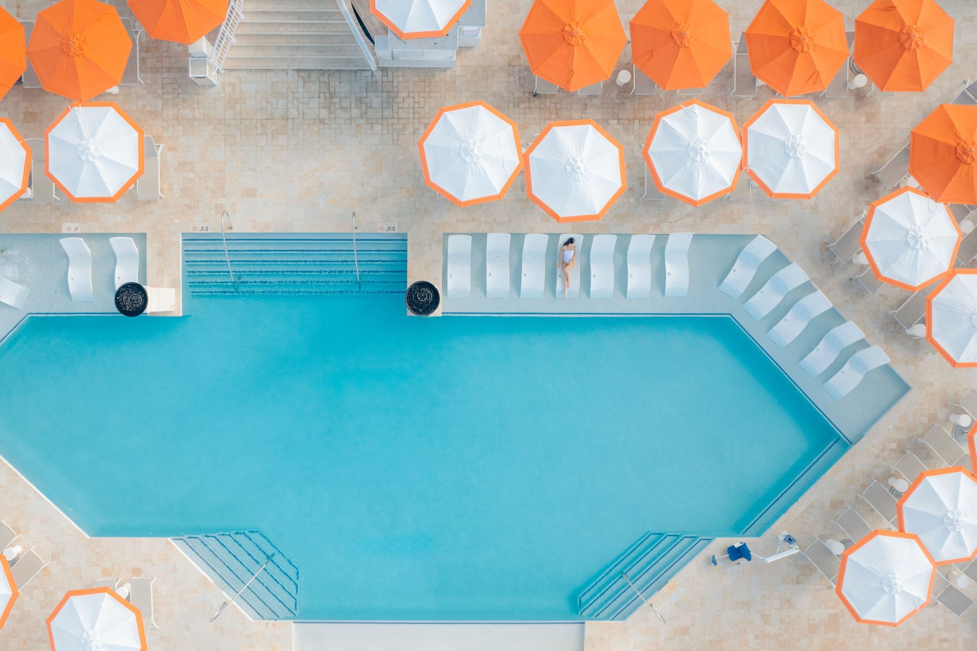 A swimming pool with multiple lounge chairs and umbrellas.