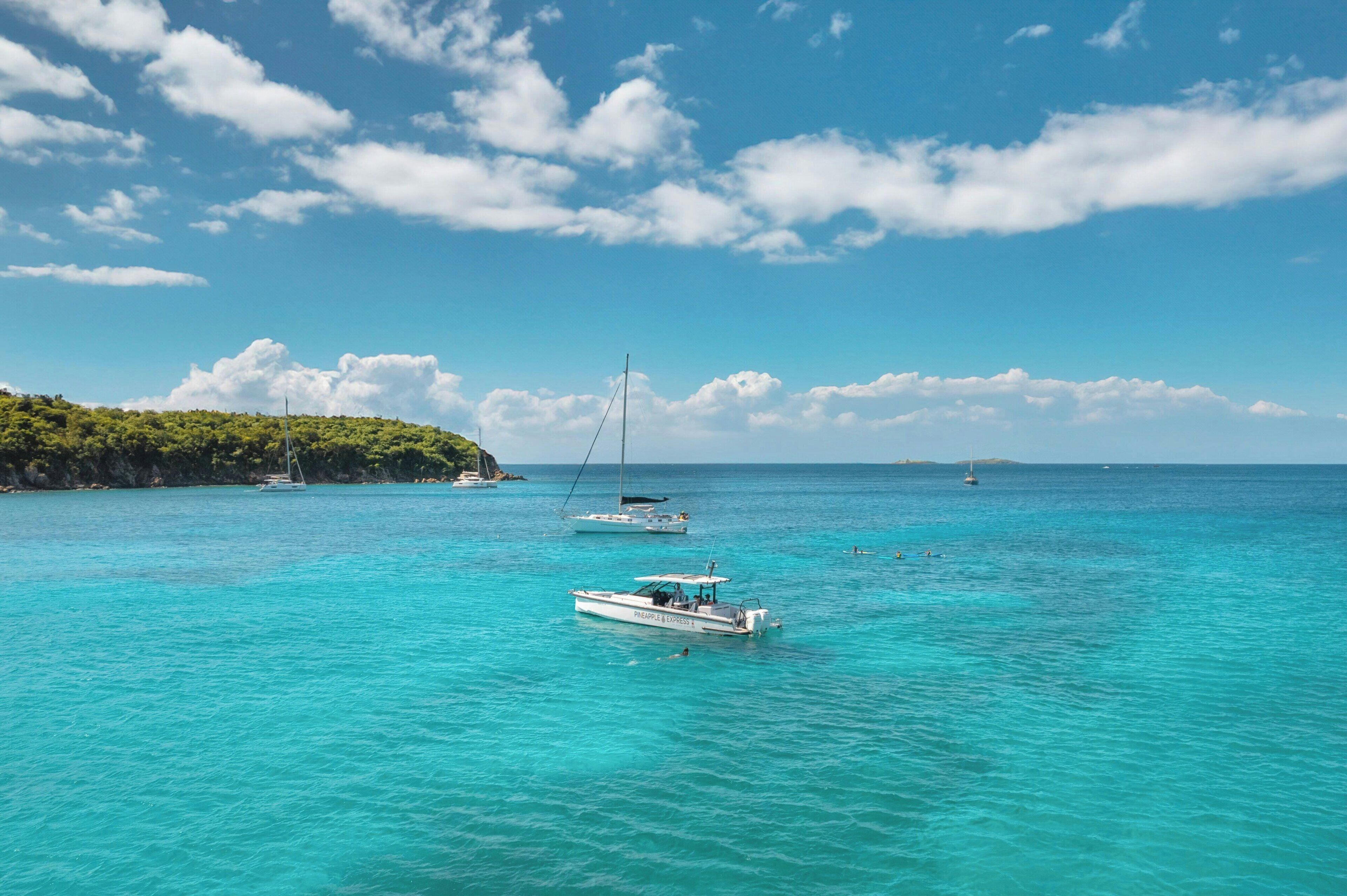 Een heldere turquoise zee met boten en een rotsachtig eiland op de achtergrond.