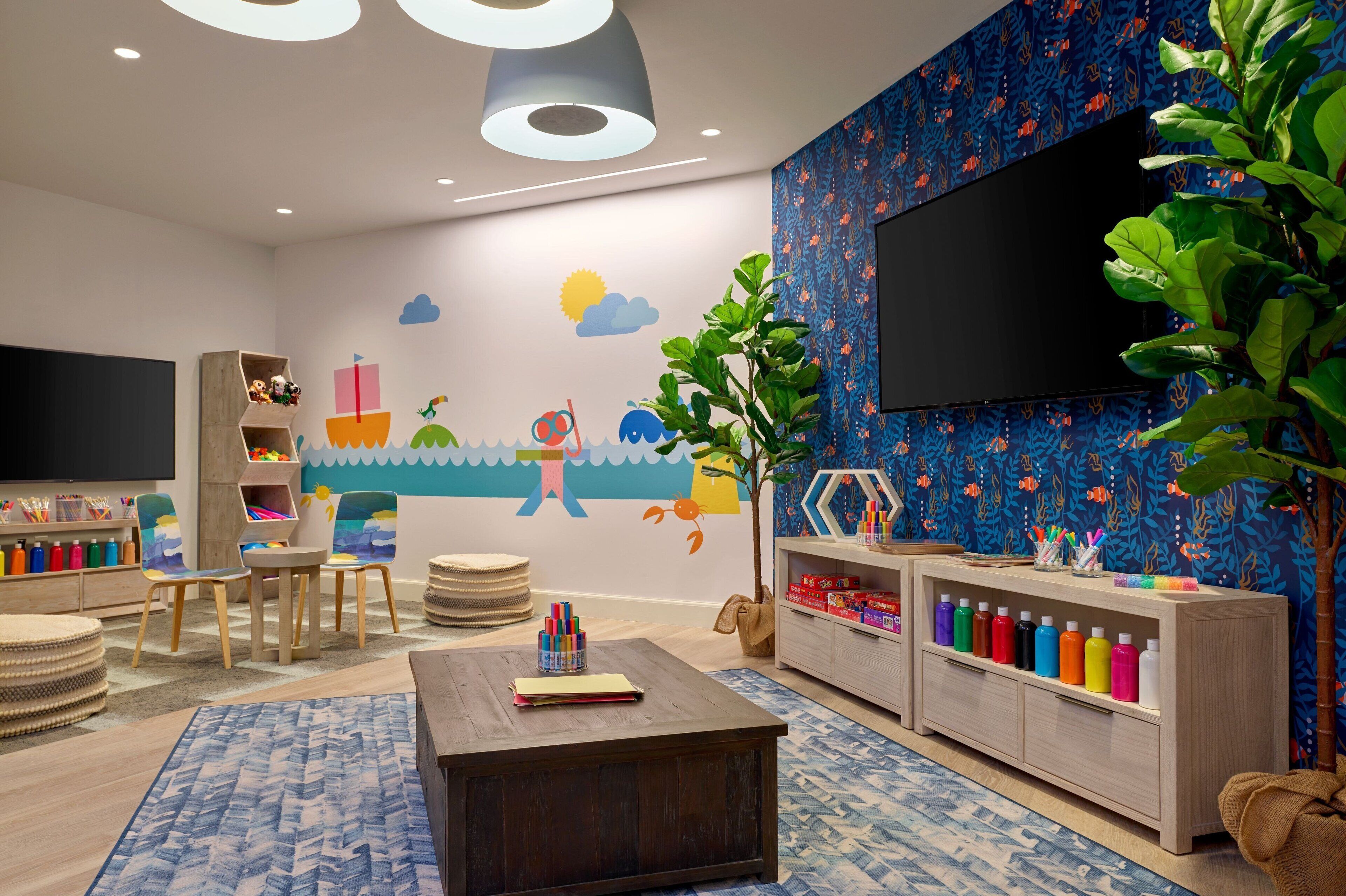 Ein kindgerechtes Zimmer mit Spielbereich, großem Fernseher und Wandgemälde.