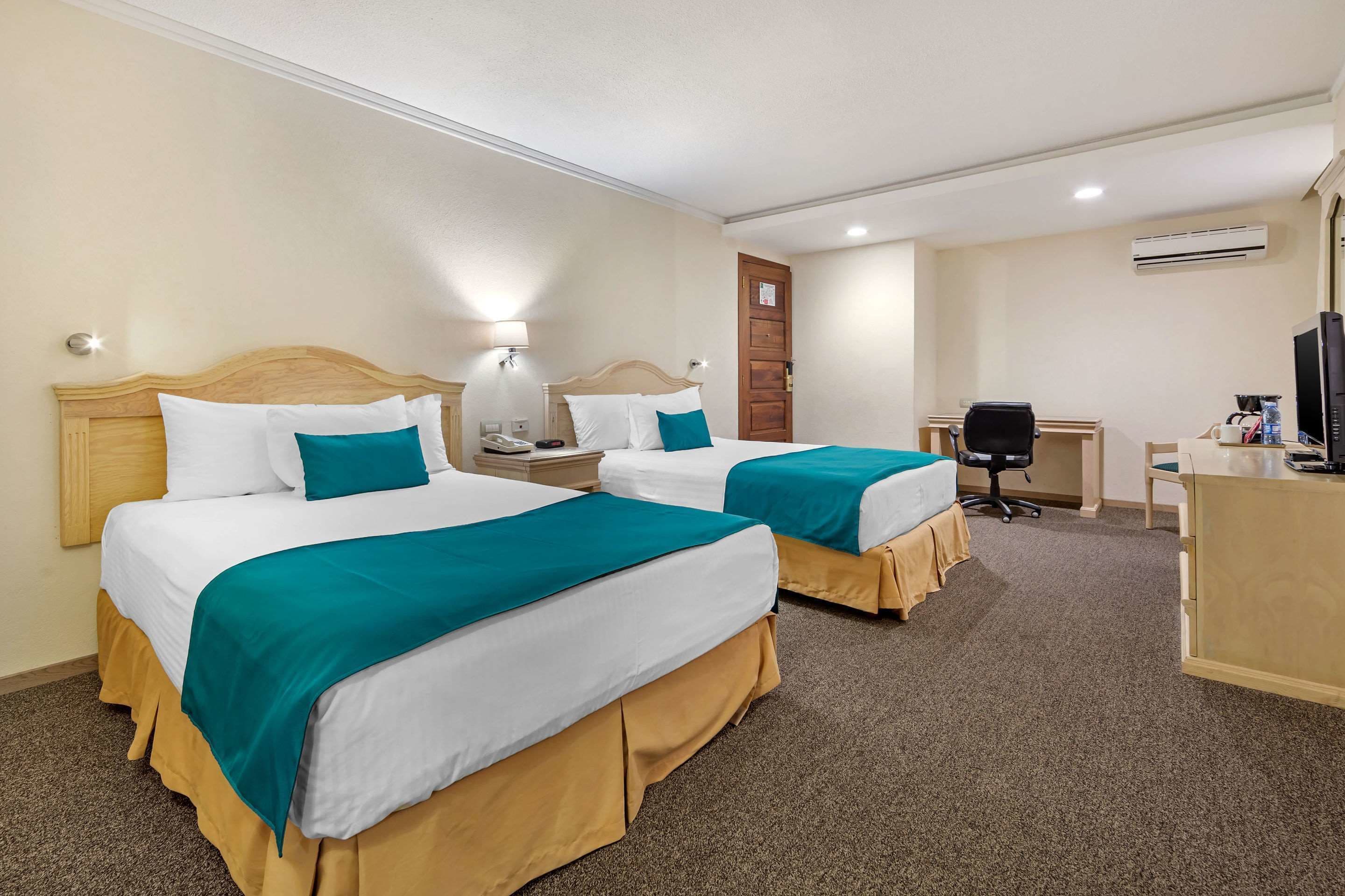 A hotel room with two beds, a desk, a chair, and a television.