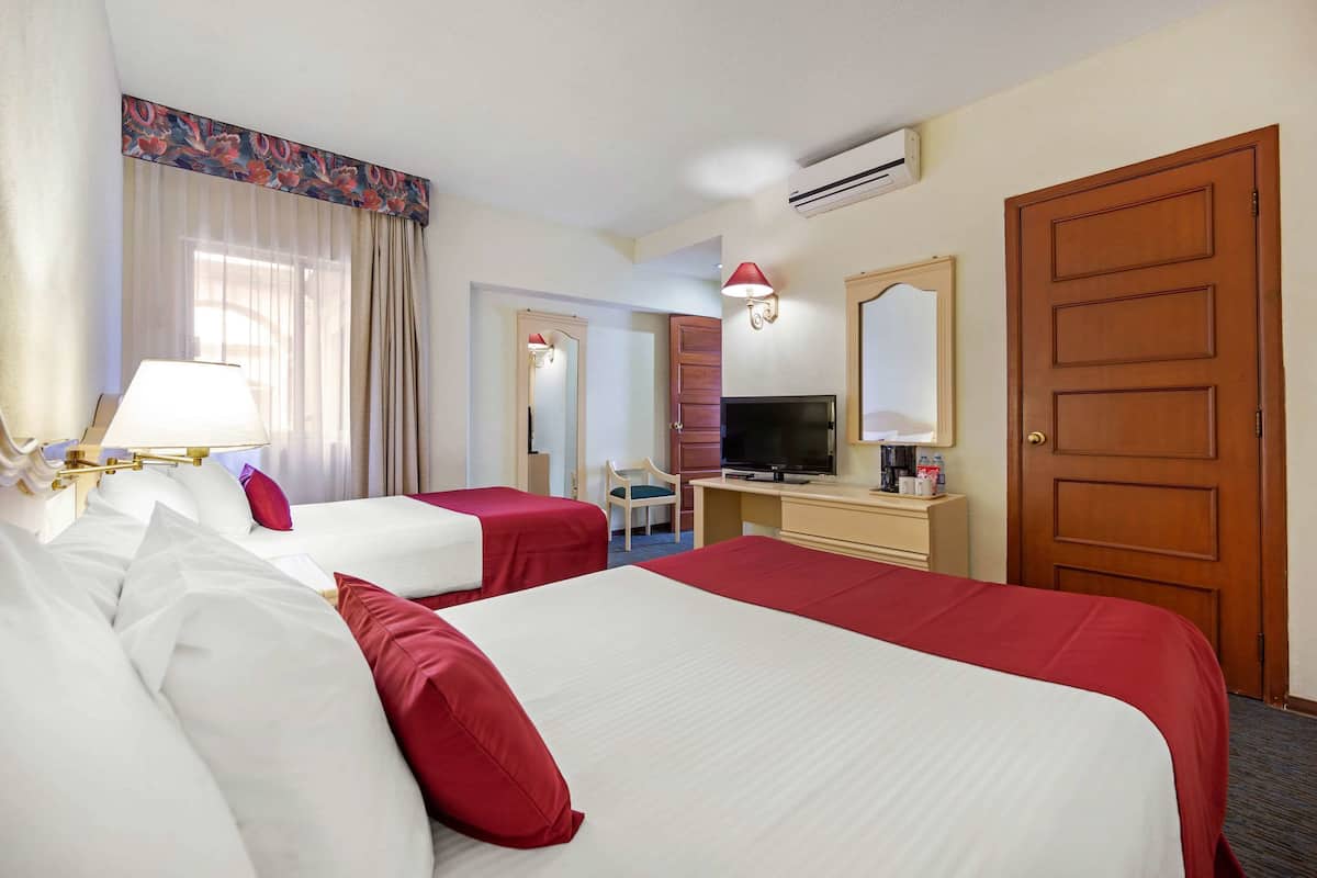 A hotel room with two beds, a desk with a TV, a mirror, and a door.