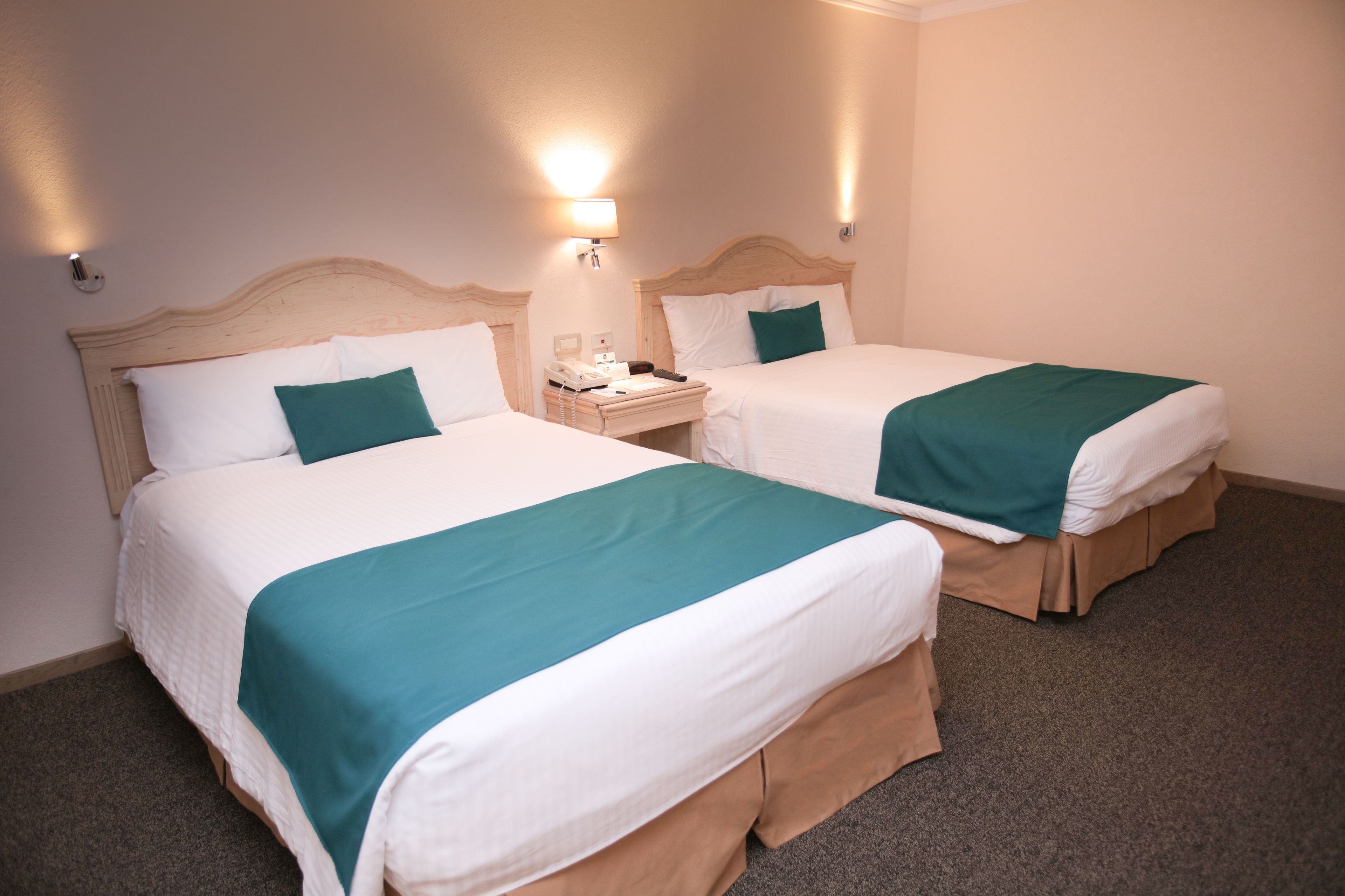 Dos camas individuales con cabeceros de madera, ropa de cama blanca y almohadones turquesa.