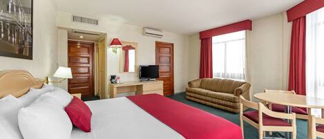 A hotel room with a bed, a desk with a television, a sofa, and a dining table.
