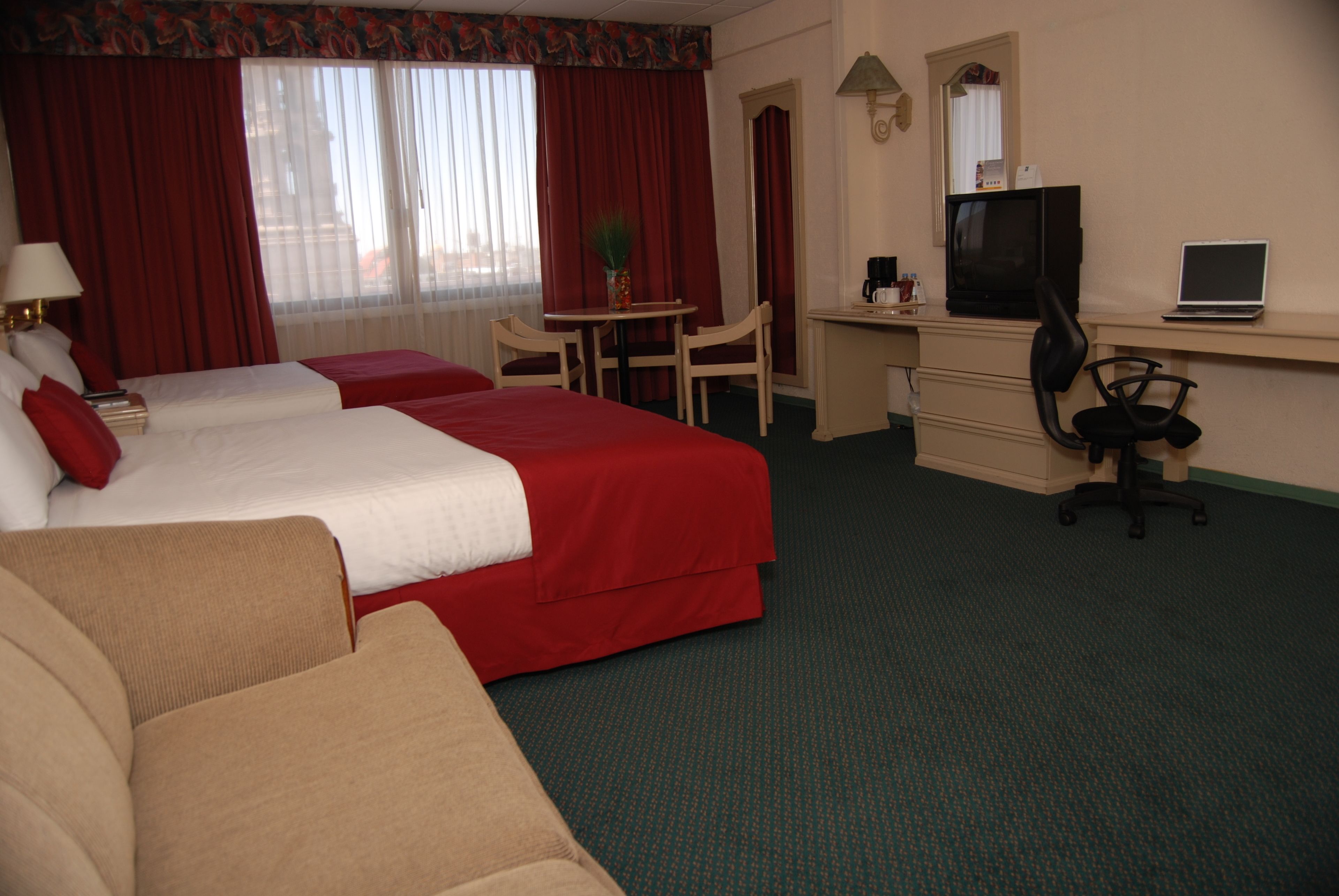 A hotel room with two beds, a desk with a computer, a TV, and a chair.