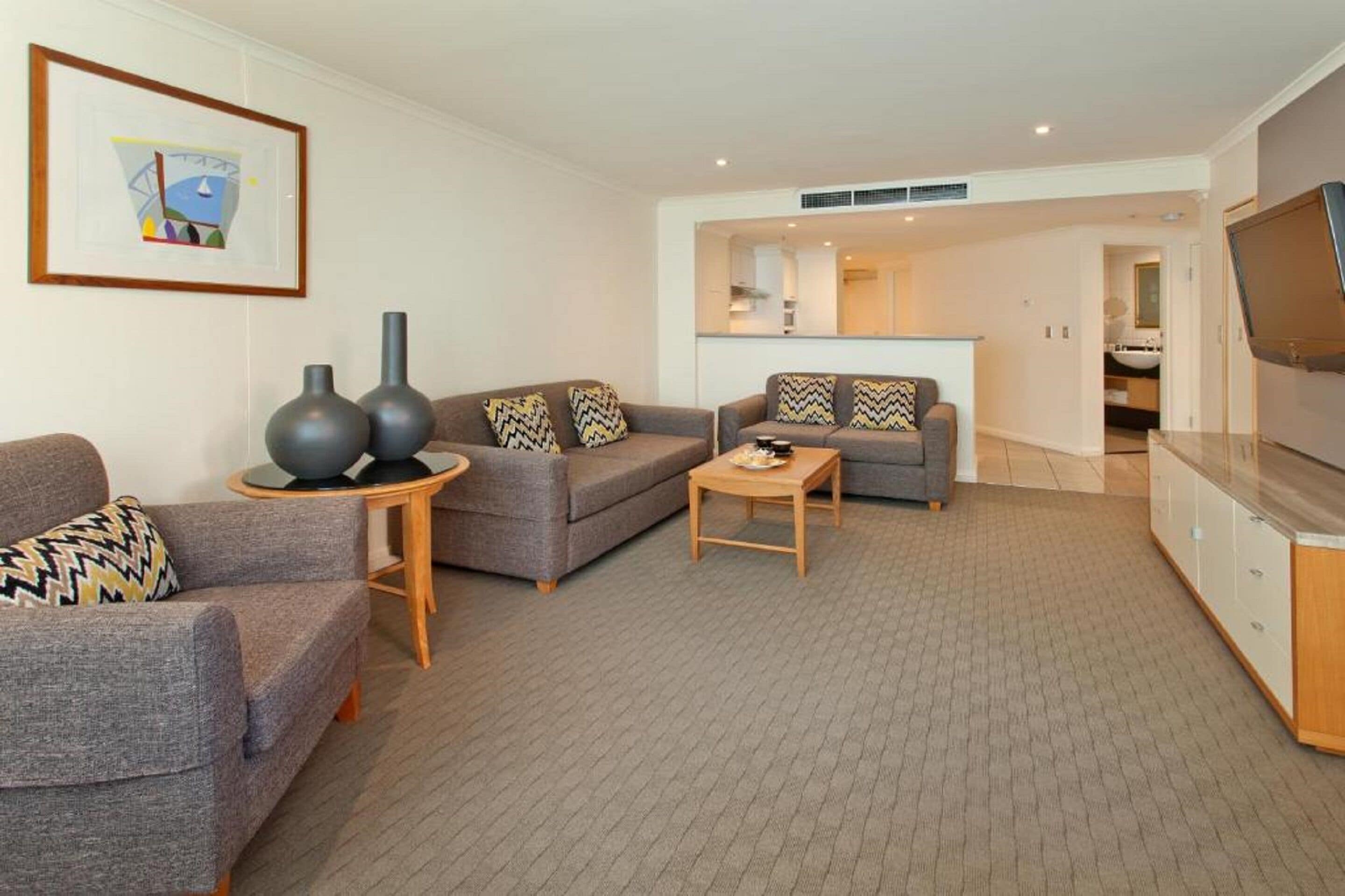 A modern living room with grey sofas, a coffee table, and a TV. There is a framed picture on the wall and a vase on a side table.