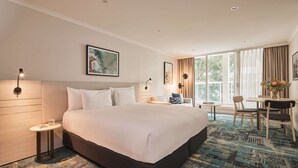 A hotel room with a large bed, a small side table, a desk with chairs, and a view of the outdoors through large windows. - Rydges Darling Square Apartment Hotel (Sydney)