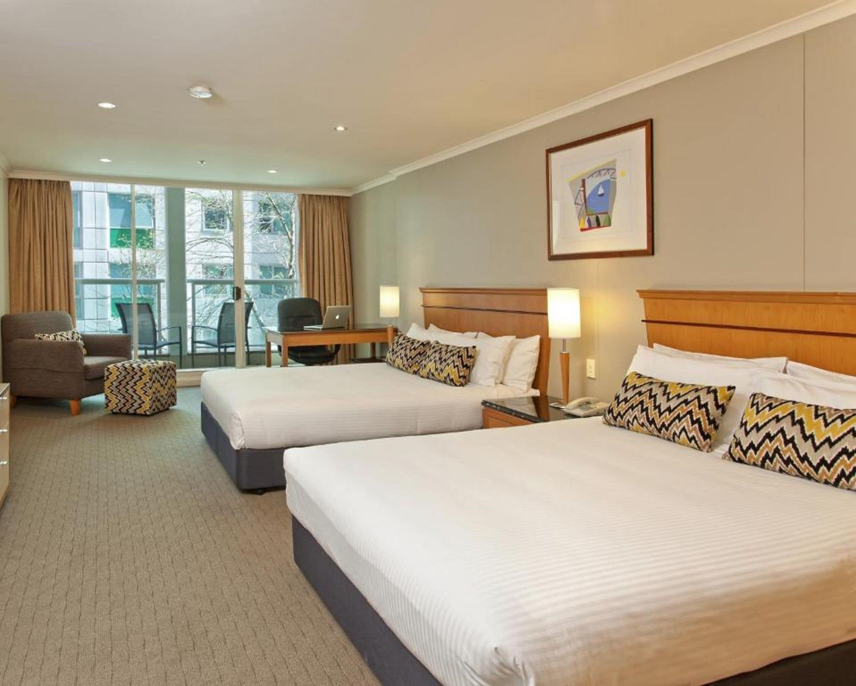 A hotel room with two beds, a desk, a chair, and a window with curtains.