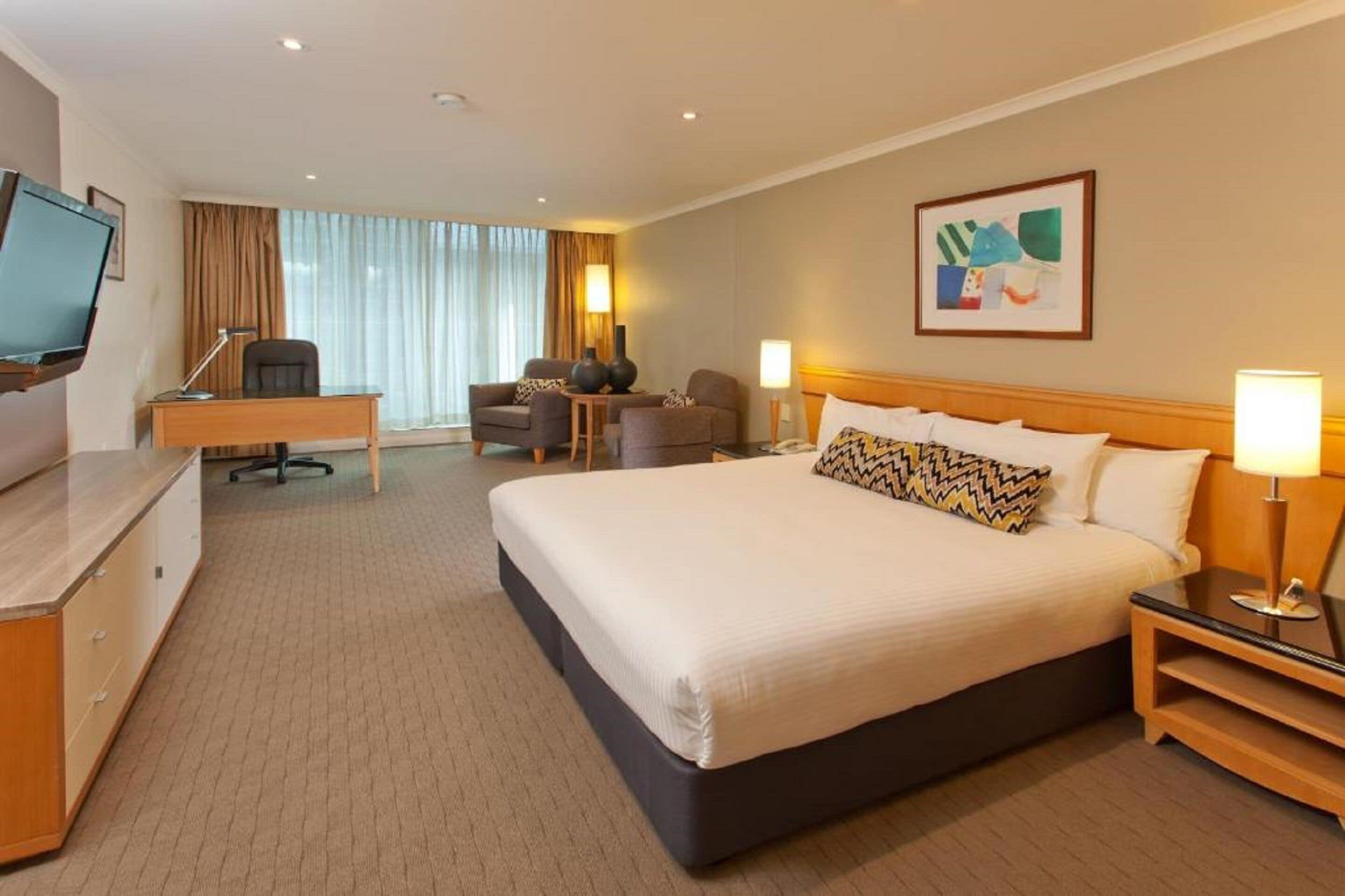 Une chambre d’hôtel avec un grand lit, un bureau, une chaise, une télévision et un tableau au mur.