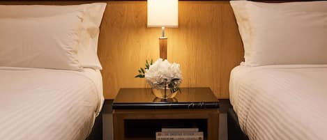 Quarto de hotel com duas camas, uma mesa de cabeceira com abajur e um vaso com flores.