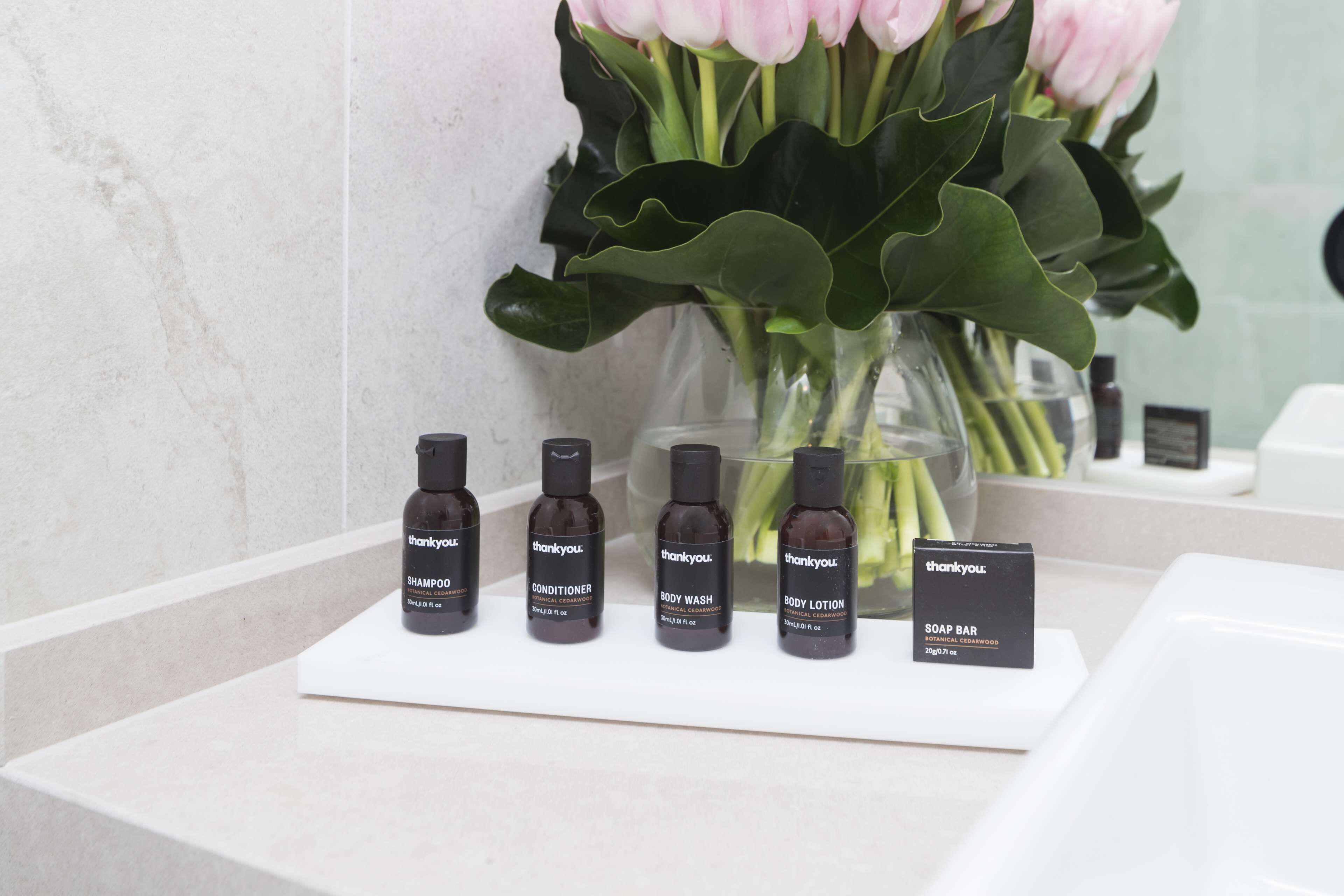 A bathroom counter with a selection of Thankyou brand toiletries including shampoo, conditioner, body wash, body lotion, and soap bar.