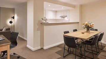 A modern dining area with a wooden table and black chairs, a small side table with a vase, and a kitchen in the background.