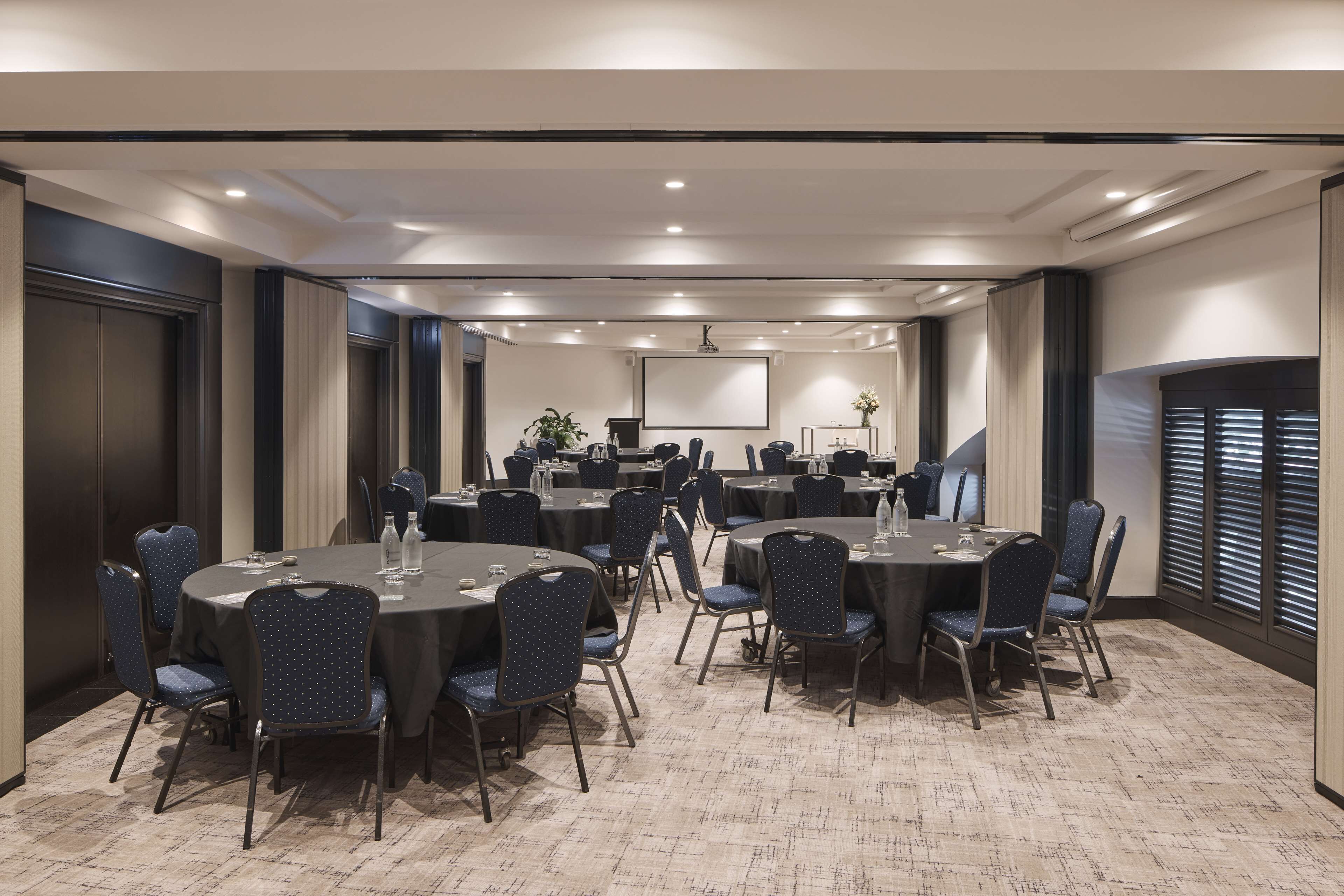 A conference room with round tables, chairs, and a large screen at the front.
