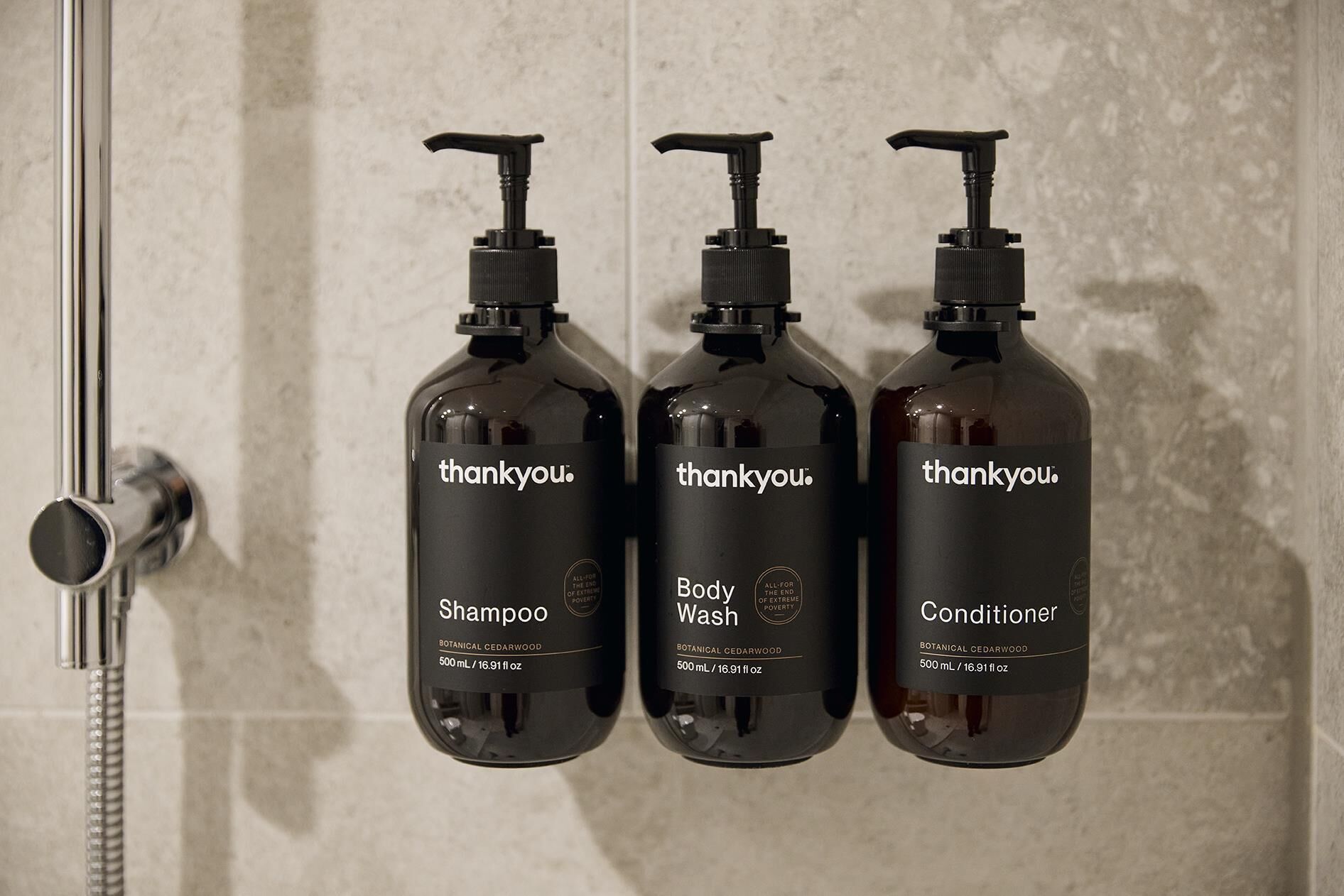 Drei Flaschen Thankyou Duschgel, Shampoo und Conditioner, sowie ein Duschkopf auf der linken Seite.