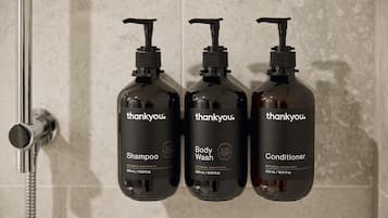 Drei Flaschen Thankyou Duschgel, Shampoo und Conditioner, sowie ein Duschkopf auf der linken Seite.